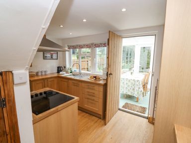 A kitchen with wooden cabinets a stove a sink and an open door leading to a dining area at Newbury Cottage in Bourton-On-The-Water