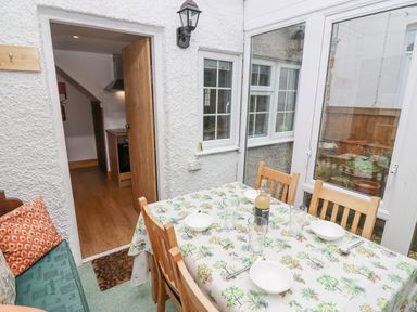A dining area with a table set with bowls and glasses next to windows and a door at Newbury Cottage in Bourton-On-The-Water