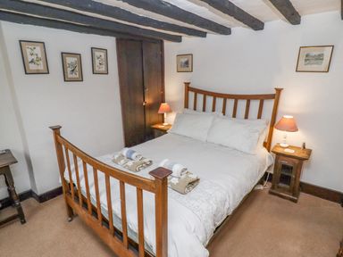 A bedroom with a wooden bed frame white bedding bedside tables with lamps and framed pictures on the walls at Newbury Cottage in Bourton-On-The-Water