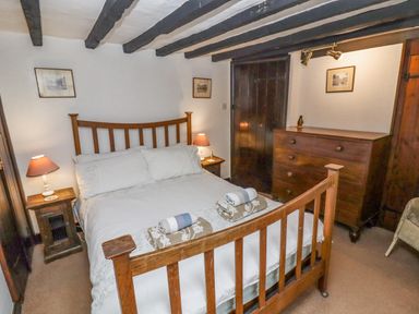 A bedroom with a wooden bed frame bedside tables lamps a wooden dresser and framed pictures at Newbury Cottage in Bourton-On-The-Water