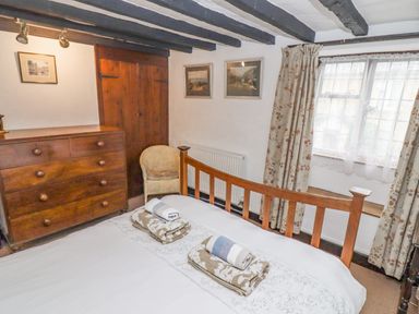 A bedroom with a wooden bed and chest of drawers with towels on the bed at Newbury Cottage in Bourton-On-The-Water
