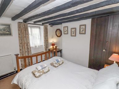 A bedroom with a wooden bed frame two bedside tables with lamps floral curtains and framed pictures on the wall at Newbury Cottage in Bourton-On-The-Water