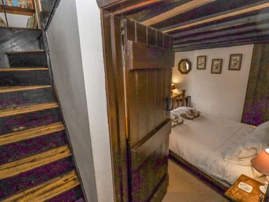 A bedroom with a wooden bed frame bedside table with a lamp framed pictures and a staircase outside the room at Newbury Cottage in Bourton-On-The-Water