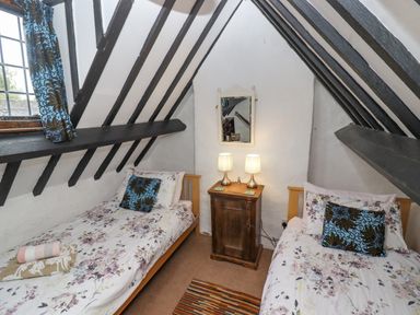 A bedroom with two single beds a wooden nightstand with two lamps and a mirror at Newbury Cottage in Bourton-On-The-Water