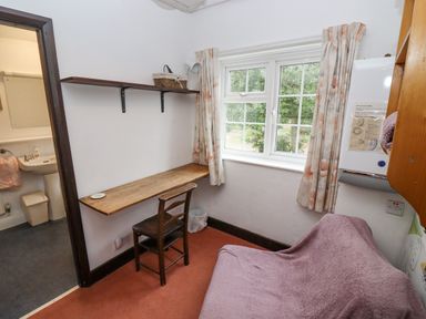 A small room with a wooden desk and chair near a window with floral curtains at Newbury Cottage in Bourton-On-The-Water