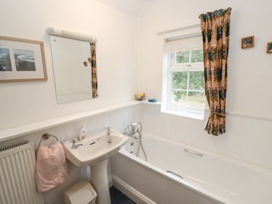 A bathroom with a bathtub sink mirror and window with a curtain at Newbury Cottage in Bourton-On-The-Water