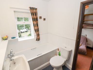 A bathroom with a bathtub sink toilet window and patterned curtain at Newbury Cottage in Bourton-On-The-Water