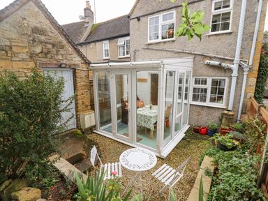 A small garden patio area with white metal table and chairs next to a glass conservatory at Newbury Cottage in Bourton-On-The-Water