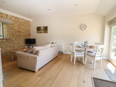 A living room with a beige sofa a wooden coffee table a small television and a dining table with four chairs at Saddlebacks Barn in Burford