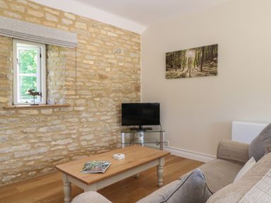 A living room with a stone wall a window a coffee table a sofa a television and a forest picture on the wall at Saddlebacks Barn in Burford