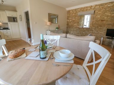 A dining table set with a bottle of wine glasses and bread near a kitchen and living area with a stone wall at Saddlebacks Barn Burford
