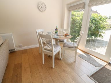 A dining area with a round wooden table and four white chairs near large windows at Saddlebacks Barn in Burford