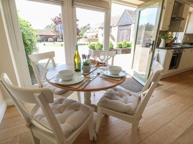 A dining area with a round table set for two and white chairs near glass doors in a kitchen at Saddlebacks Barn in Burford