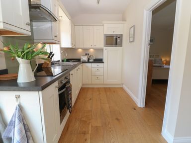 A kitchen with cabinets sink microwave oven and flowers on the counter at Saddlebacks Barn in Burford