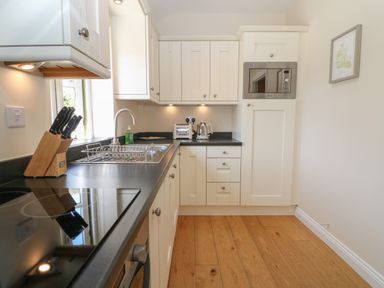 A kitchen with white cabinets black countertops a sink a microwave toaster kettle and a knife block at Saddlebacks Barn in Burford