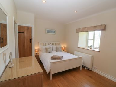 A bedroom with a double bed bedside tables a dresser a window and a wooden door at Saddlebacks Barn in Burford