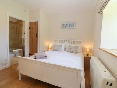 A bedroom with a white bed and bedside lamps next to an ensuite bathroom at Saddlebacks Barn in Burford