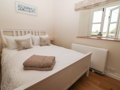 A bedroom with a white bed a window with a vase on the sill and a folded towel on the bed at Saddlebacks Barn in Burford