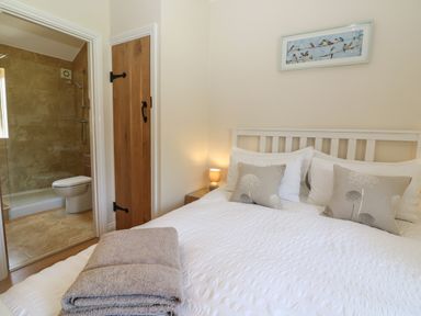 A bedroom with a bed white bedding two pillows folded towels nightstand lamp door to bathroom with shower toilet Saddlebacks Barn Burford