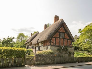 A thatched cottage with trees and a fence at Elmhurst Cottage in Lower Quinton