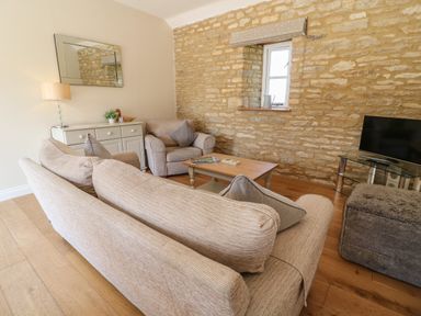 A living room with sofas a coffee table a television on a stand and a sideboard against a stone wall at Ewecub Barn in Burford