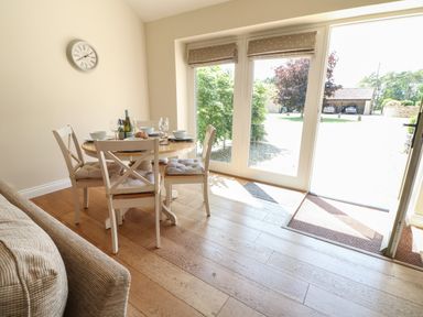 A dining area with a round table set for four and glass doors leading outside at Ewecub Barn in Burford