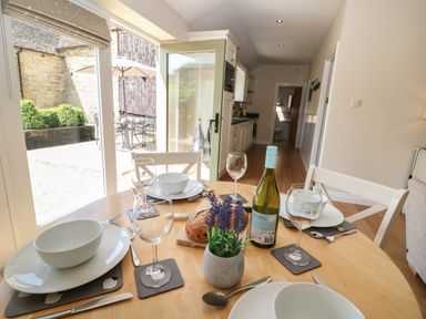 A dining table set with plates glasses cutlery and a wine bottle in a kitchen with an open door to a patio at Ewecub Barn in Burford