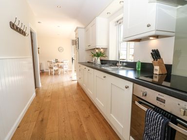 A kitchen with white cabinets a black countertop a stove a sink and a dining table at Ewecub Barn in Burford