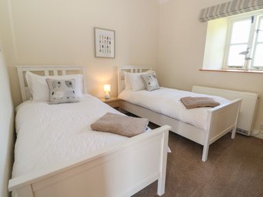 A bedroom with two single beds white bedding and sheep themed pillows at Ewecub Barn in Burford