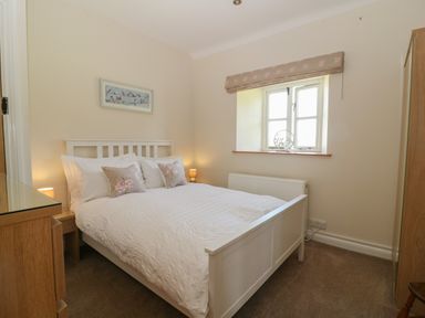 A bedroom with a white bed and floral pillows next to a window at Ewecub Barn in Burford