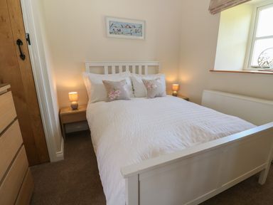A bedroom with a white bed, bedside tables with lamps, a chest of drawers, and a window at Ewecub Barn in Burford