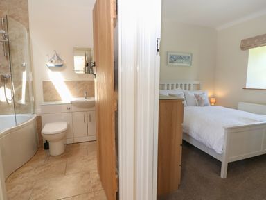 A bathroom with a toilet and shower next to a bedroom with a bed and bedside lamp at Ewecub Barn in Burford