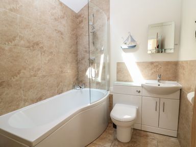 A bathroom with a bathtub shower toilet and sink with storage at Ewecub Barn in Burford