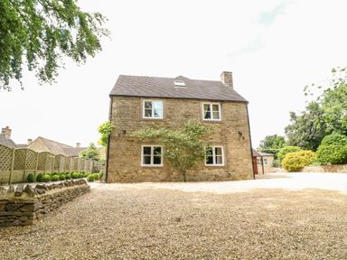 Stone house with four windows and a tree in front on a gravel driveway at South Hill Farmhouse in Stow-On-The-Wold