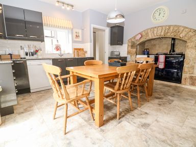 A kitchen with a wooden dining table and chairs a stone fireplace and dark cabinetry at South Hill Farmhouse in Stow-On-The-Wold
