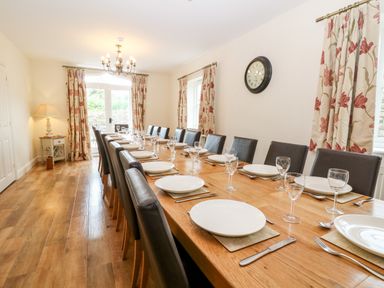 A dining room with a long wooden table set with plates and glasses at South Hill Farmhouse in Stow-On-The-Wold