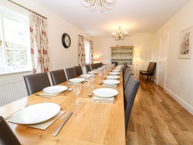 A dining room with a long wooden table set with white plates glasses and silverware surrounded by dark chairs at South Hill Farmhouse in Stow-On-The-Wold