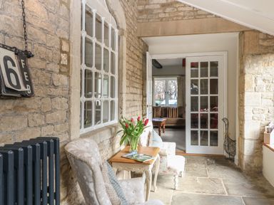 A sitting area with two chairs and a small table with flowers between two stone walls at South Hill Farmhouse in Stow-On-The-Wold