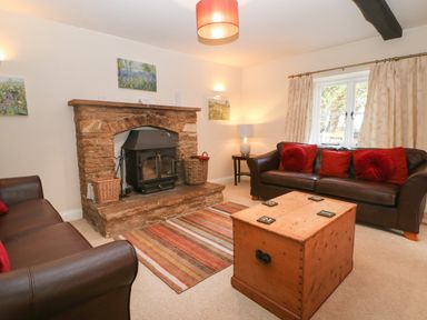 A living room with two brown leather sofas red cushions wooden chest coffee table stone fireplace and window with curtains at South Hill Farmhouse in Stow-On-The-Wold