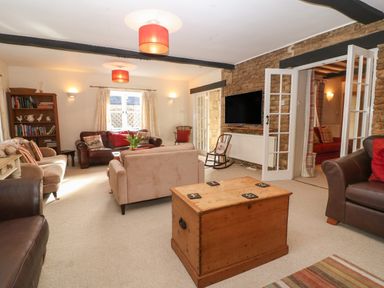 A living room with sofas a wooden chest coffee table a bookshelf and a mounted television at South Hill Farmhouse in Stow-On-The-Wold