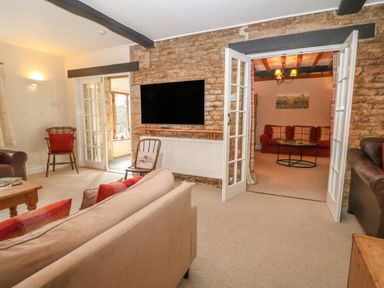 A living room with sofas chairs a mounted television and an open doorway showing another room with a sofa and a table at South Hill Farmhouse in Stow-On-The-Wold