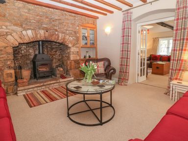 A living room with a stone fireplace wood stove red sofas and a round table with flowers at South Hill Farmhouse in Stow-On-The-Wold