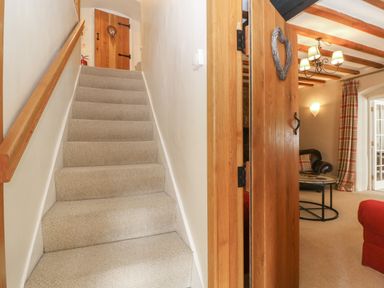 Carpeted staircase next to wooden door leading to a room with a coffee table and armchair at South Hill Farmhouse in Stow-On-The-Wold