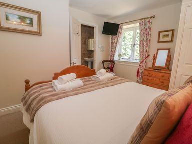 A bedroom with a wooden bed a chest of drawers a chair and a window with floral curtains at South Hill Farmhouse in Stow-On-The-Wold