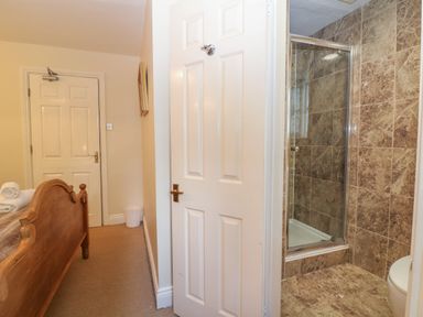 A bedroom with a wooden bed and an open door revealing a tiled shower area at South Hill Farmhouse in Stow-On-The-Wold