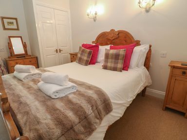A bedroom with a wooden bed with folded towels and cushions and a dresser with a mirror at South Hill Farmhouse in Stow-On-The-Wold