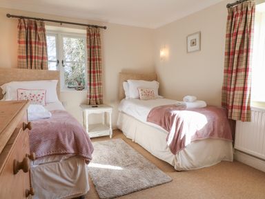 A bedroom with two single beds pink blankets and a white bedside table at South Hill Farmhouse in Stow-On-The-Wold