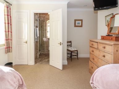 A bedroom with an open door leading to a bathroom a wooden dresser a chair and a wall-mounted television at South Hill Farmhouse in Stow-On-The-Wold