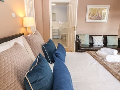 A bedroom with a bed with pillows and folded towels a lamp a sofa with cushions and a painting on the wall at South Hill Farmhouse in Stow-On-The-Wold