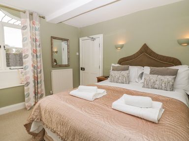 A bedroom with a double bed with pillows folded towels window with patterned curtains and a mirror on the wall at South Hill Farmhouse in Stow-On-The-Wold